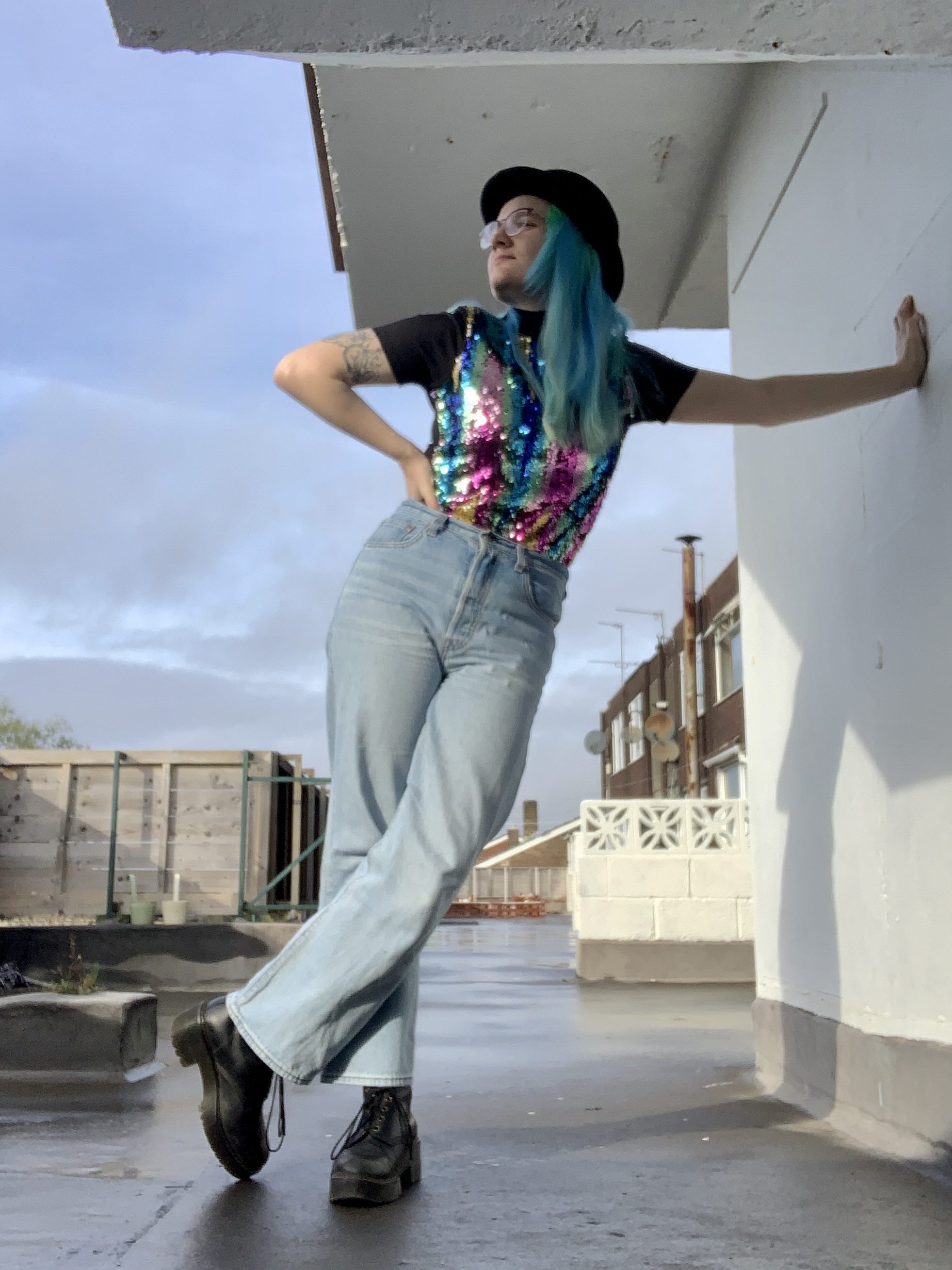 Portrait photograph of a fabulous non-binary person with blue hair, a bowler hat and lots of sparkles